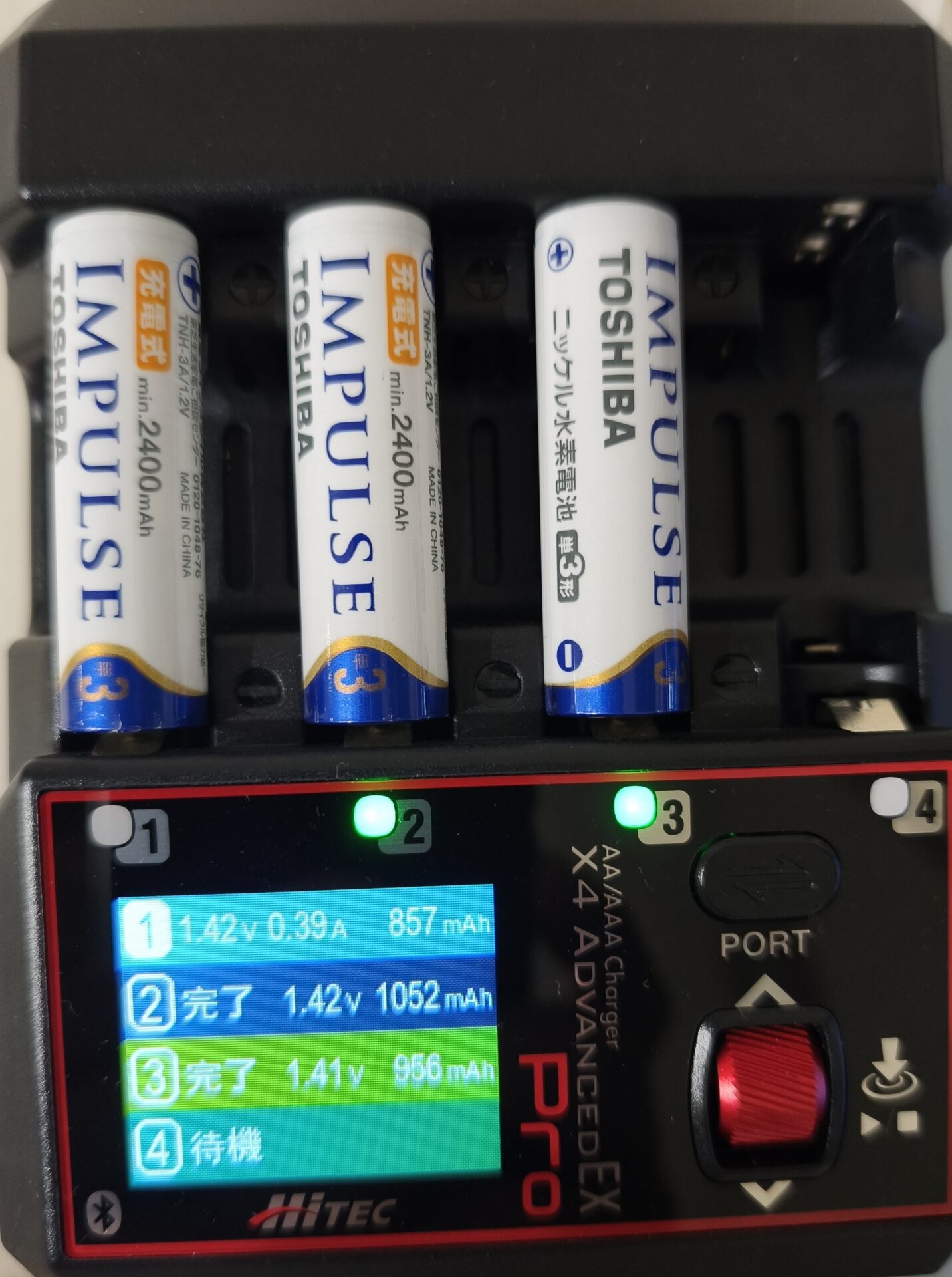 Hitec X4 Advanced EX Proの充電モード画面、撮影途中の様子。スロット1は進行中で1.42V 0.39A 857mAh、スロット2は完了で1.42V 1052mAh、スロット3は完了で1.41V 956mAh、スロット4は電池なしで待機